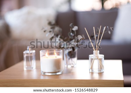 decoration, hygge and aromatherapy concept - aroma reed diffuser, burning candle, branches of eucalyptus populus and perfume on table at home