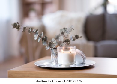 Decoration, Hygge And Cosiness Concept - Burning White Fragrance Candle On Tray And Branches Of Eucalyptus Populus On Table At Cozy Home