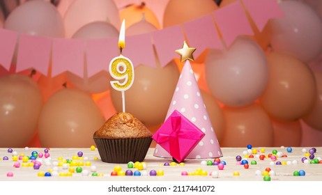Decorations with balloons and a happy birthday candle with the number 9 for a child. Happy birthday greetings in pink colors for a nine-year-old child for a girl, copy space. Muffin
