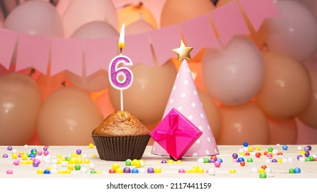 Decorations with balloons and a happy birthday candle with the number 6 years old for a child. Happy birthday greetings in pink colors for a six year old child for a girl, copy space. Muffin 
