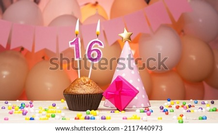 Decorations with balloons and a happy birthday candle with the number 16 for a child. Happy birthday greetings in pink colors for a sixteen-year-old child for a girl, copy space. Muffin with a burning
