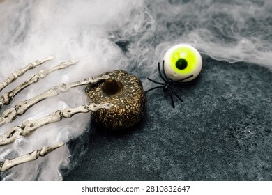 Decorations for Halloween include a small pumpkin with a hole a fake spider and a spooky eye surrounded by white fluff on a dark surface.