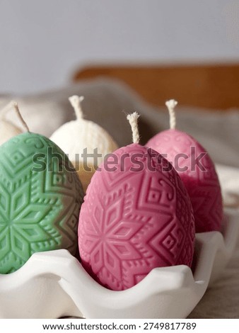 Decorative beeswax candles in the shape of Easter eggs with ethnic patterns in pink and green colors. Festive spring home decor. Vertical close-up.