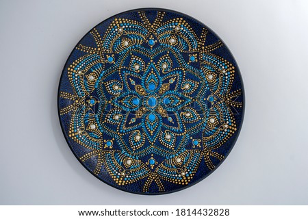 Decorative ceramic plate with black, blue and golden colors, painted plate on white background, closeup, top view. Decorative porcelain plate painted with acrylic paints, handwork, dot painting