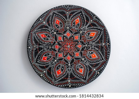 Decorative ceramic plate with red and silver colors, painted plate on white background, closeup, top view. Decorative porcelain plate painted with acrylic paints, handwork, dot painting