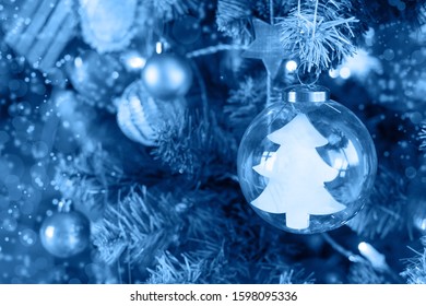 Decorative Christmas tree on a light background with shiny balls and a glass ball inside which is a Christmas tree with copyspace in classic blue. trend color