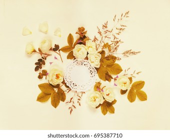 Decorative Composition In Retro Style Consisting Of Round White Paper Openwork Doily And White Wild Rose Flowers With Green Leaves On White Background. Top View, Flat Lay. Mocap. Toned Image