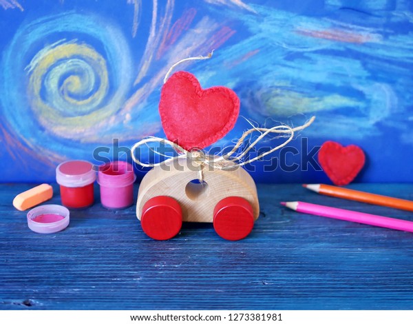 Decorative composition of a toy car and a\
heart made of felt, paints and pencils on the background of pastel\
drawing, the concept of congratulations on Valentine\'s Day, holiday\
decorations, greeting 