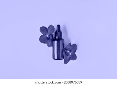 Decorative cosmetics composition of serum mockup bottle decorated with orchid flowers. Toned in trendy color of year 2022. Natural cosmetics concept. Flat lay style. Copy space.