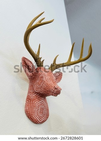 Decorative deer head wall mount sculpture with red and white tribal geometric dot pattern and realistic antlers, displayed indoors.