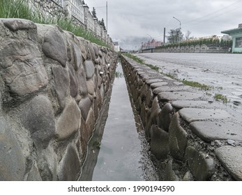 Decorative Drain Ditch With Walls Lined With Stone Boulders Near The Road, Close-up.