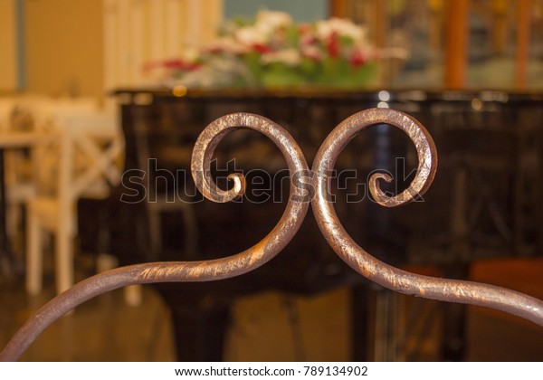 Decorative\
element made of bronze, handmade. Interior of an old cafe,\
restaurant, salon. In the background, a black grand piano, white\
tables and chairs. The background is\
blurred.