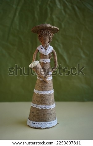 Decorative figure made of straw in the form of woman with flowers. Girl doll in hat with flowers made of handmade threads. DIY. Souvenir toy on green background. Selective focus