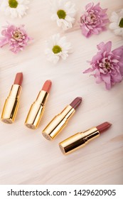Decorative flat lay composition with cosmetics lipstick and flowers. Top view on white wood background
