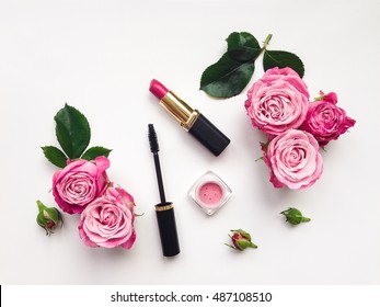 Decorative flat lay composition with mascara, lipstick and blush, decorated with flowers. Top view on white background, view from above