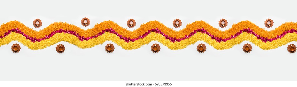 Decorative Flower rangoli Strip or Border or Pattern for Diwali or Pongal Festival made using marigold or zendu flowers and red rose petals over white background with Clay Oil Lamps, selective focus