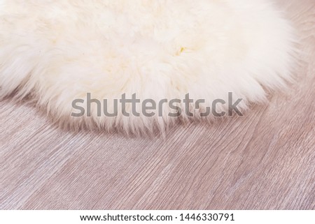 Decorative fur carpet on wood floor background. White animal skin on the parquet floor in the apartment. Mat made of natural skin.