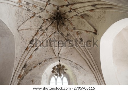 Decorative gothic vaulted ceiling with painted patterns and hanging chandelier inside medieval stone church.