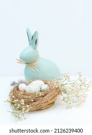 Decorative Hare, Easter Bunny And Easter Eggs In Straw On A Light Background With Copy Space. Vertical Easter Photo.