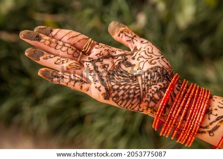 A decorative henna or mehndi design on a female's hand wearing red bangles