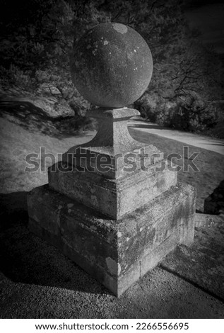 Decorative historic aged stone ball finial on top of square layered masonry in black and white