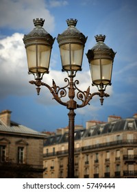 Decorative lamps against a partly cloudy sky outside of Notre Dame Cathedral in Paris, France, with buildings in the background.