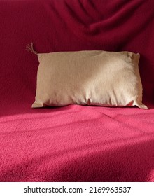 Decorative Pillow With Funny Tassel Is Casually Thrown On Sofa. Beige On Dark Red. Drapery Folds, Shadows, Sunlight. Spectacular Theme For Interior Design. Copy Space. Vertical Photo.
