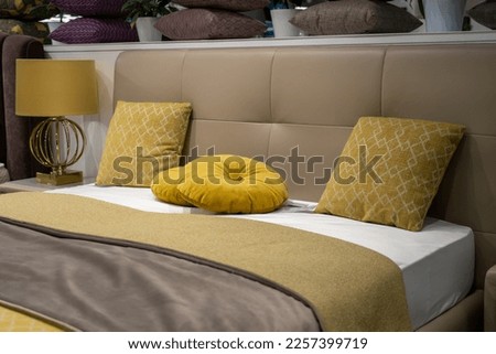 Decorative pillows on cozy bed with leather ocher colored headboard with gold brass lamp on bedside table in elegant bedroom in morning.