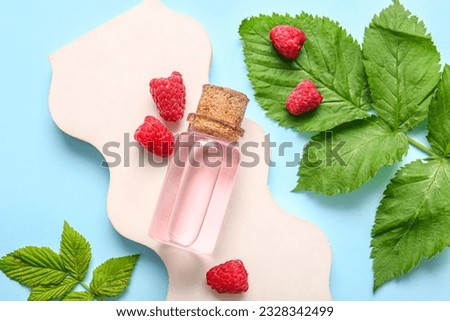 Decorative podium with bottle of cosmetic raspberry oil on blue background