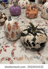Decorative pumpkins in various patterns, including floral, leaf, and checkered designs, displayed on a festive tablecloth. A perfect autumn or Halloween themed craft and decor.