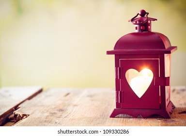 Decorative red metal lantern with a heart cutout lit by a glowing candle with copyspace for Valentines or Christmas - Powered by Shutterstock