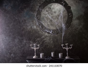 Decorative Round Frame Above Candles And Candelabras On Eerie Cobweb Covered Mantle In Haunted House Setting