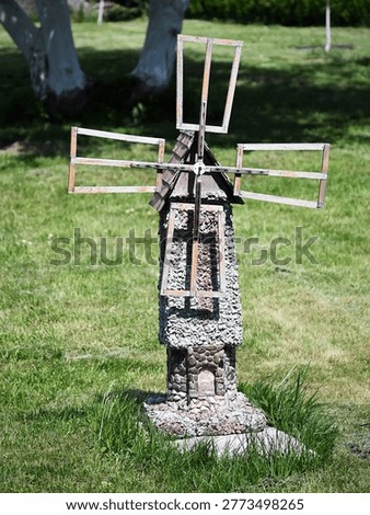 Decorative rustic garden windmill made of small stones. Unique stone and wood craft ornament for backyard decoration against a green lawn