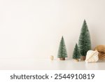 Decorative side view setup with mini snow-covered Christmas trees and paper ornaments in a Scandinavian minimalist style, placed against a neutral backdrop