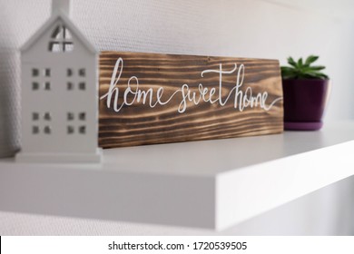 Decorative sign house sweet home from a burnt tree on a white shelf with a toy house and a flower pot, selective focus
