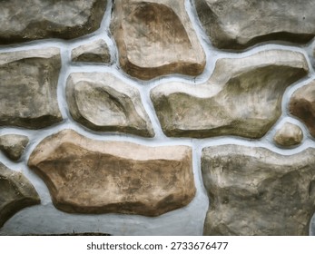 A decorative stone wall features large grey and brown rocks set in white grout. This textured masonry design creates a rustic and sturdy facade, ideal for modern architectural outdoor surfaces.