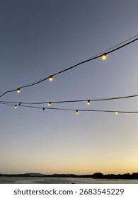 Decorative string lights glowing against a clear evening sky during sunset, creating a warm and inviting atmosphere.
