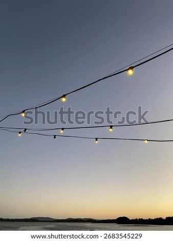 Decorative string lights glowing against a clear evening sky during sunset, creating a warm and inviting atmosphere.