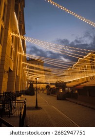 Decorative string lights hanging above a calm city street at dusk.