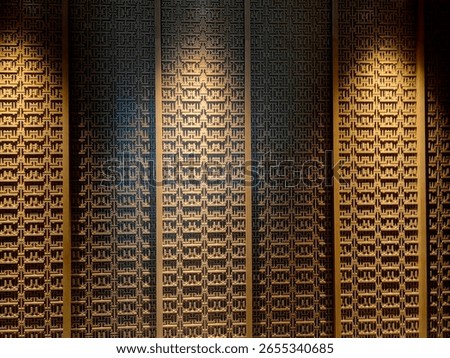 a decorative wall panel with an intricate, repeating pattern of traditional Asian  designs, and illuminated by spotlights
