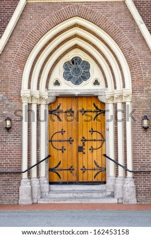 Decorative wooden entrance door with fittings in arch shaped wall recess of a Church
