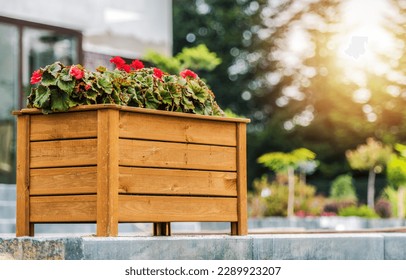 Decorative Wooden Planter Box with Blooming Red Flowers Arranged in the Residential Backyard Garden. Landscaping Design Ideas.