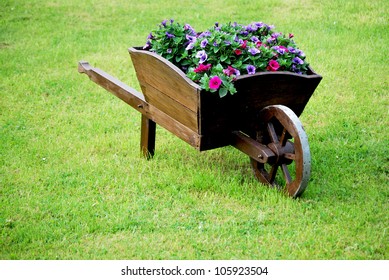 decorative wooden wheelbarrow with flowers in green grass