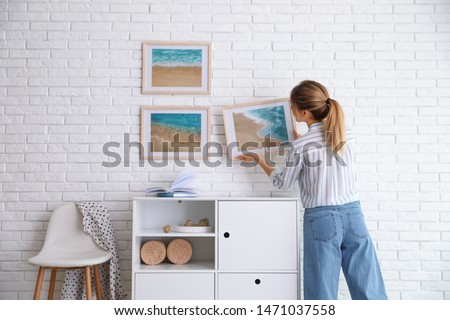 Decorator hanging picture on white brick wall in room. Interior design