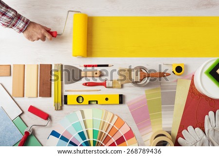 Decorator holding a painting roller and painting a wooden surface, work tools and swatches at bottom, banner with copy space Imagine de stoc © 