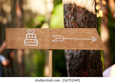 Decoratoration Wooden Wedding Cake Arrow Sign In The Pine Forest. Cake Banner On Event Venue In The Woods Outdoors.