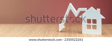 Decrease in property value. Reducing the cost of housing. Banner with a model of a white house and a graphic arrow pointing down close-up on a red background. copy space.