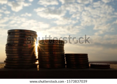 A decreasing stack of coins at sunset showing financial loss concept