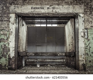Decrepit, grungy and forgotten industrial elevator with peeling paint and trash in an abandoned blue collar factory