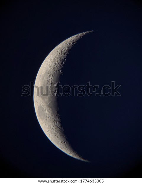 Decrescent moon with the blue sky as a backgroud.\
A small part of the surface of the moon is beeing seen, as the\
earth\'s shadow\
passes.